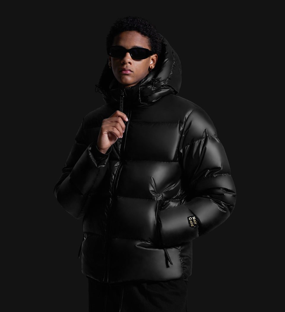 young man wearing zipped up winter puffer jacket facing an angle with sun glasses on